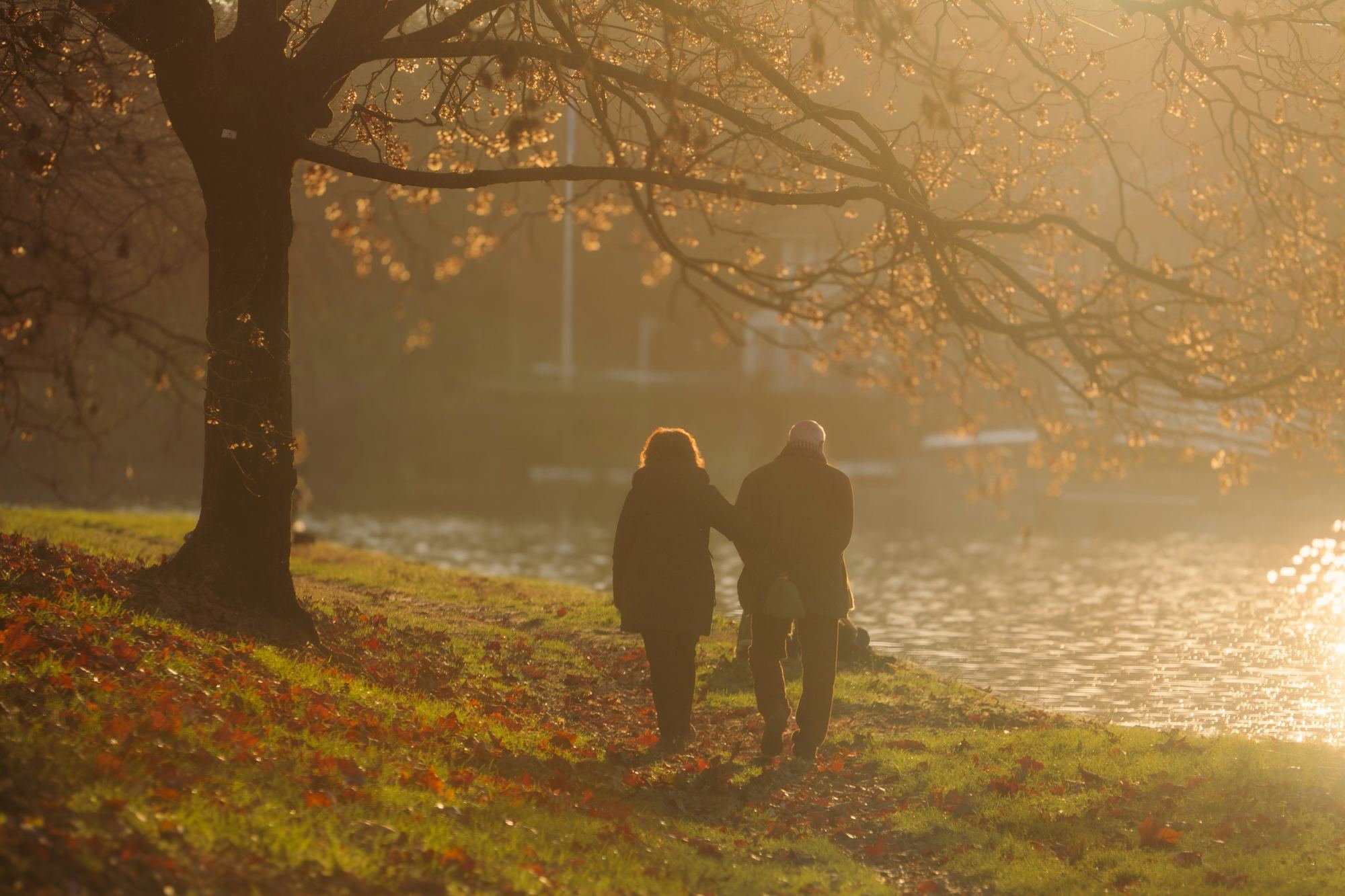 Two people walking along a river in low autumn light